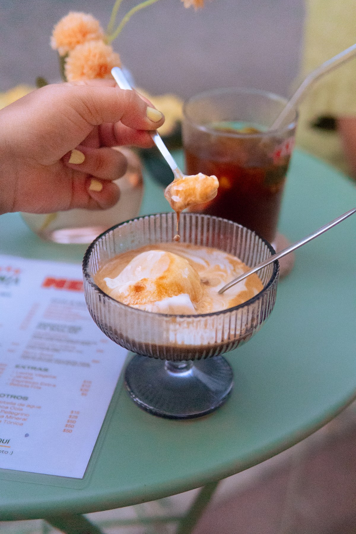 Hand with pastel yellow nails lifting a dripping spoonful of vanilla ice cream and espresso from a ribbed glass coupe
